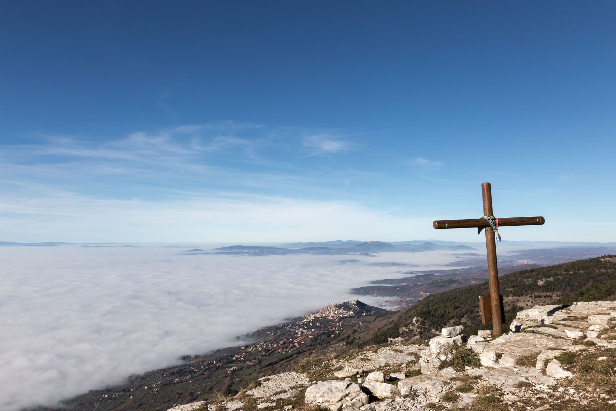 A wooden cross on top of Subasio mountain, with a sea of fog below and Assisi town (Umbria) in the background. Photo: Getty