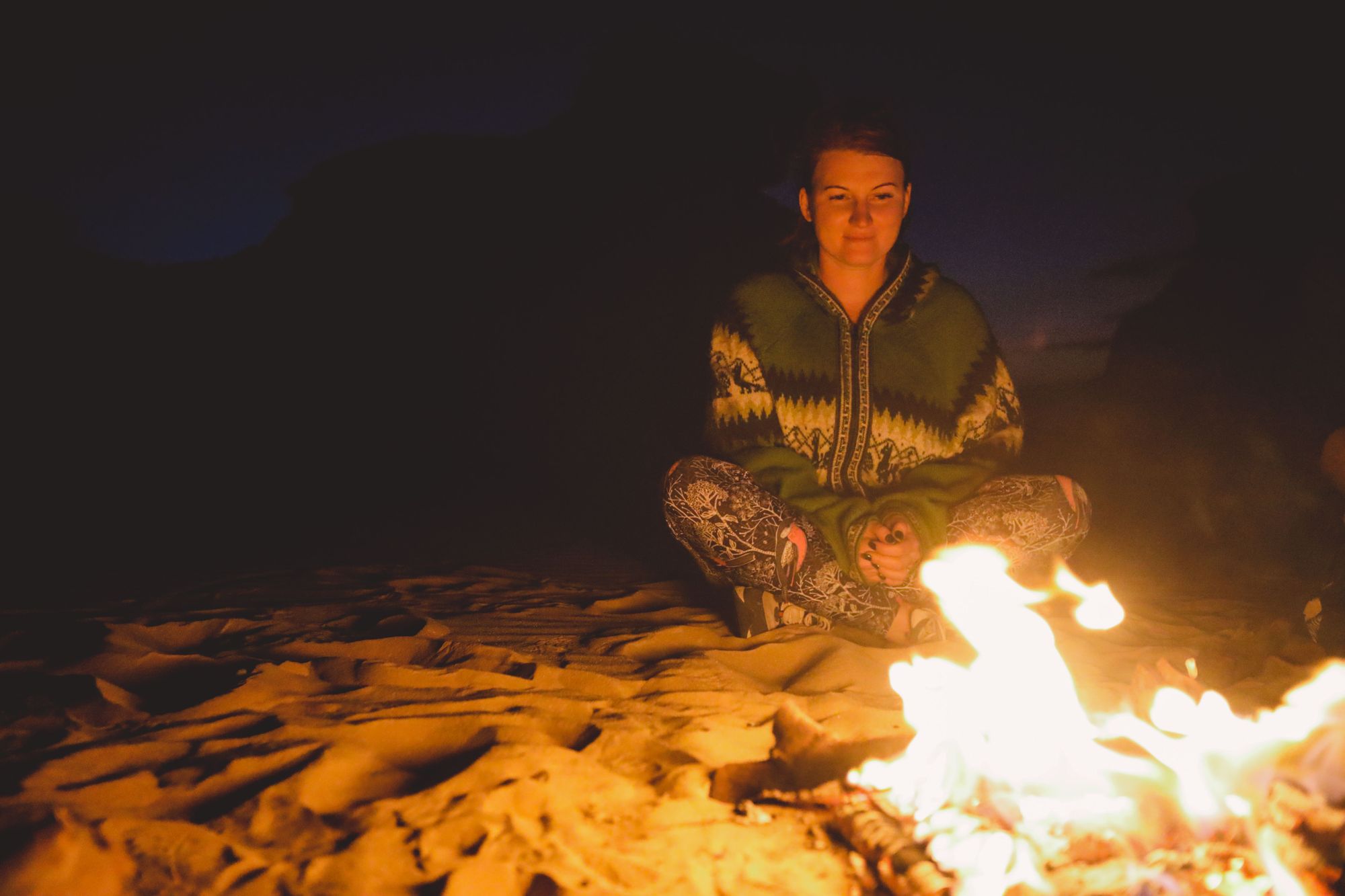 A woman sits by a campfire in the desert.