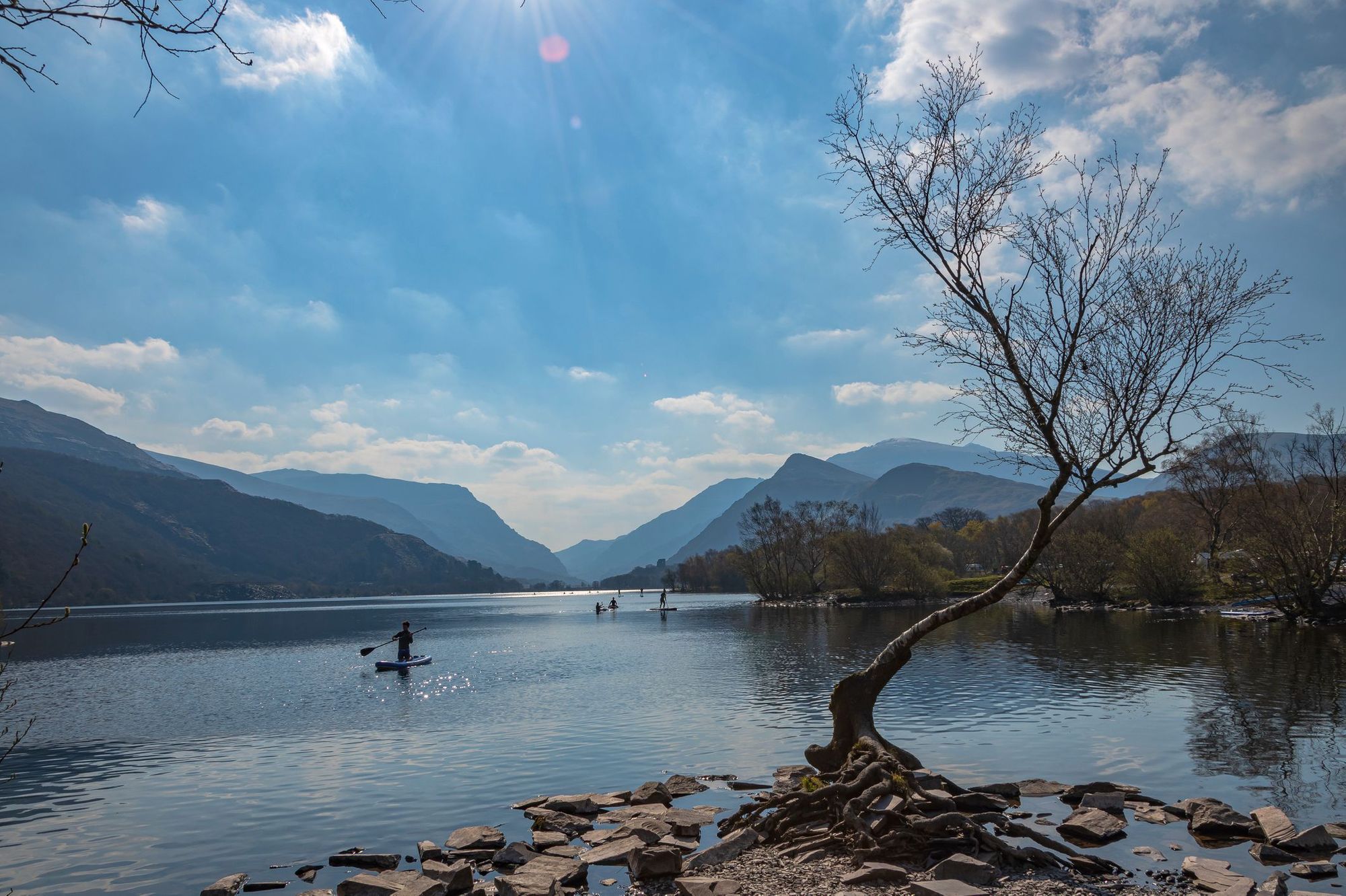 A group head out to paddle on the glimmering water of Lyln Padarn on a sunny day.