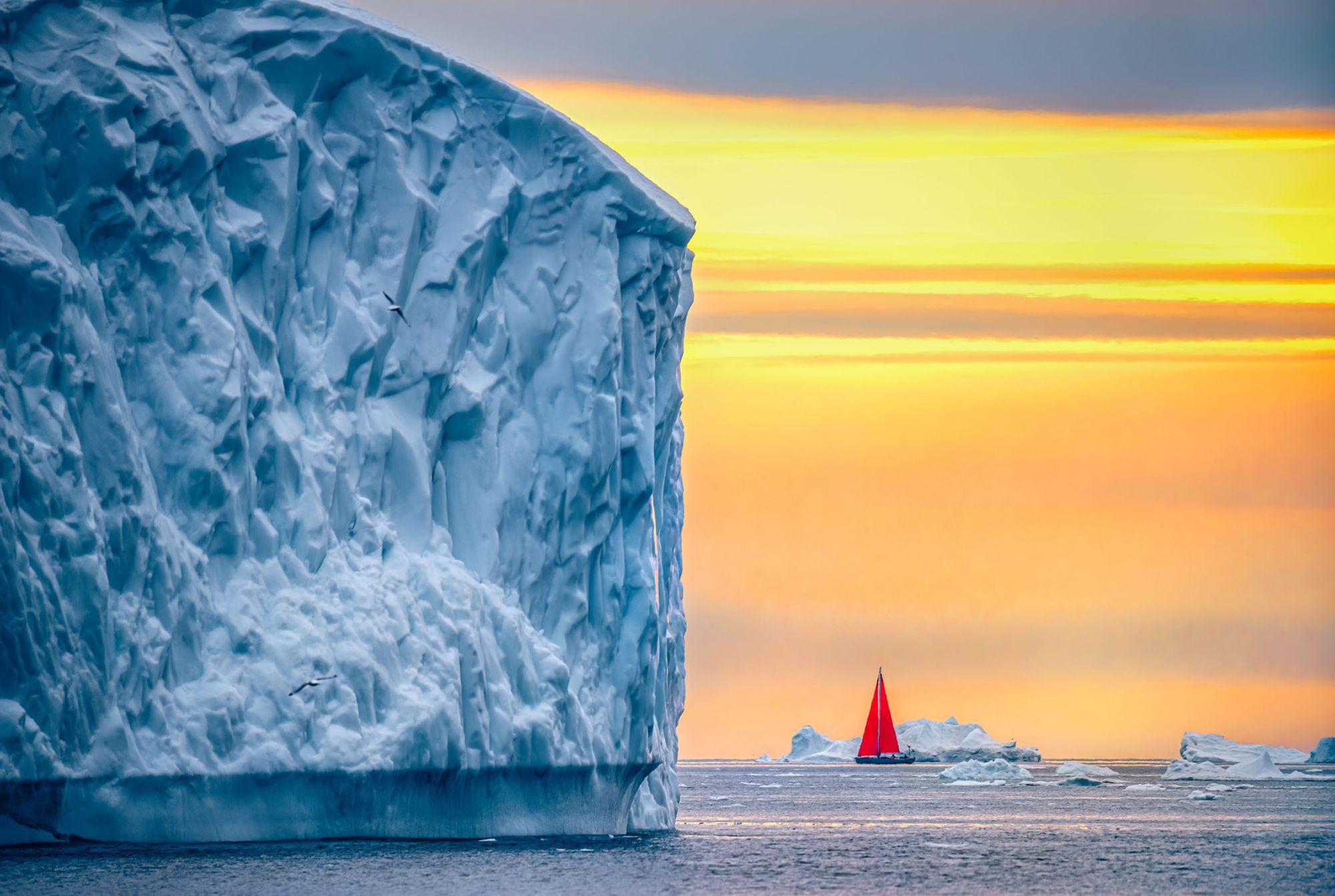 A red boat sails amongst the midnight sun of Greenland. The aurora. could be in the sky, but would not be visible. Photo: Getty