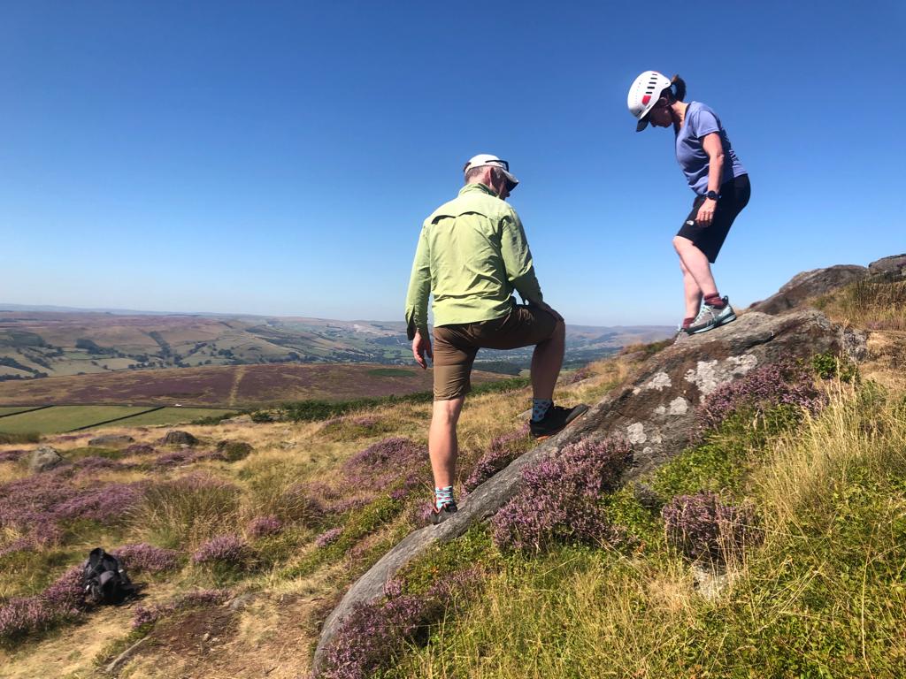 A man leads a woman down a boulder, helping her overcome a fear of heights.