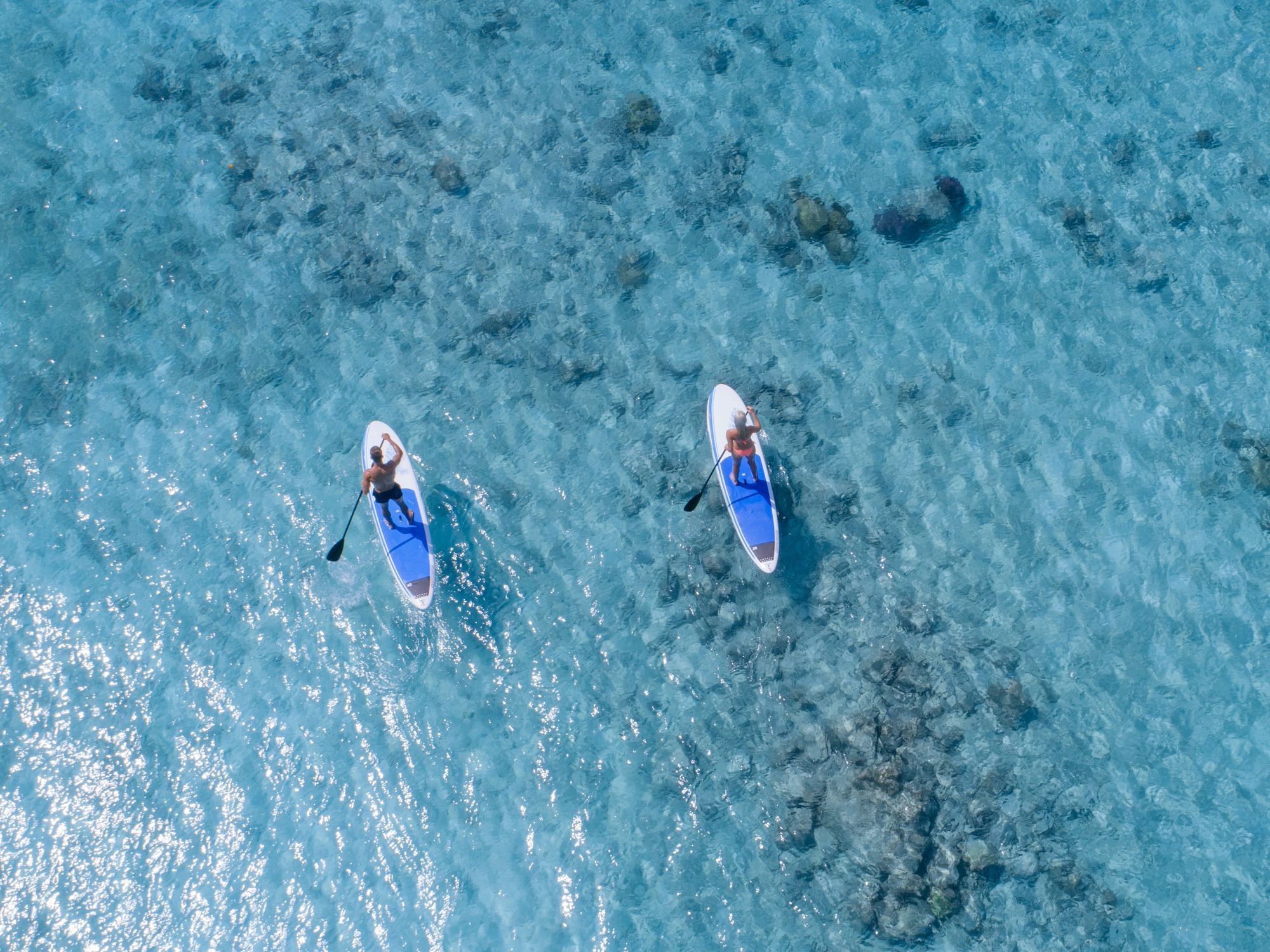 Aerial view of two paddleboarders on the clear blue waters around the Maldives.