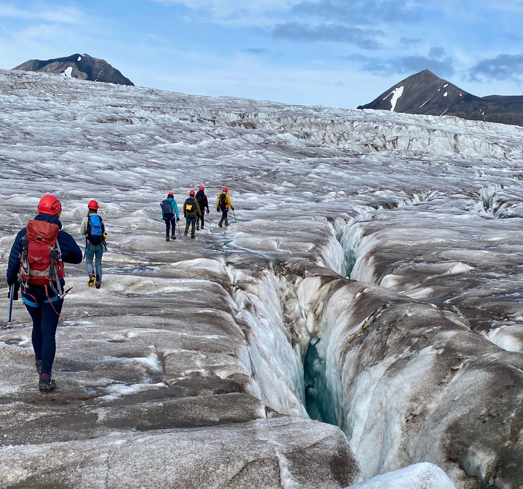 A group of hikers climbing over the Esmark Glacier next to an ice crevasse.