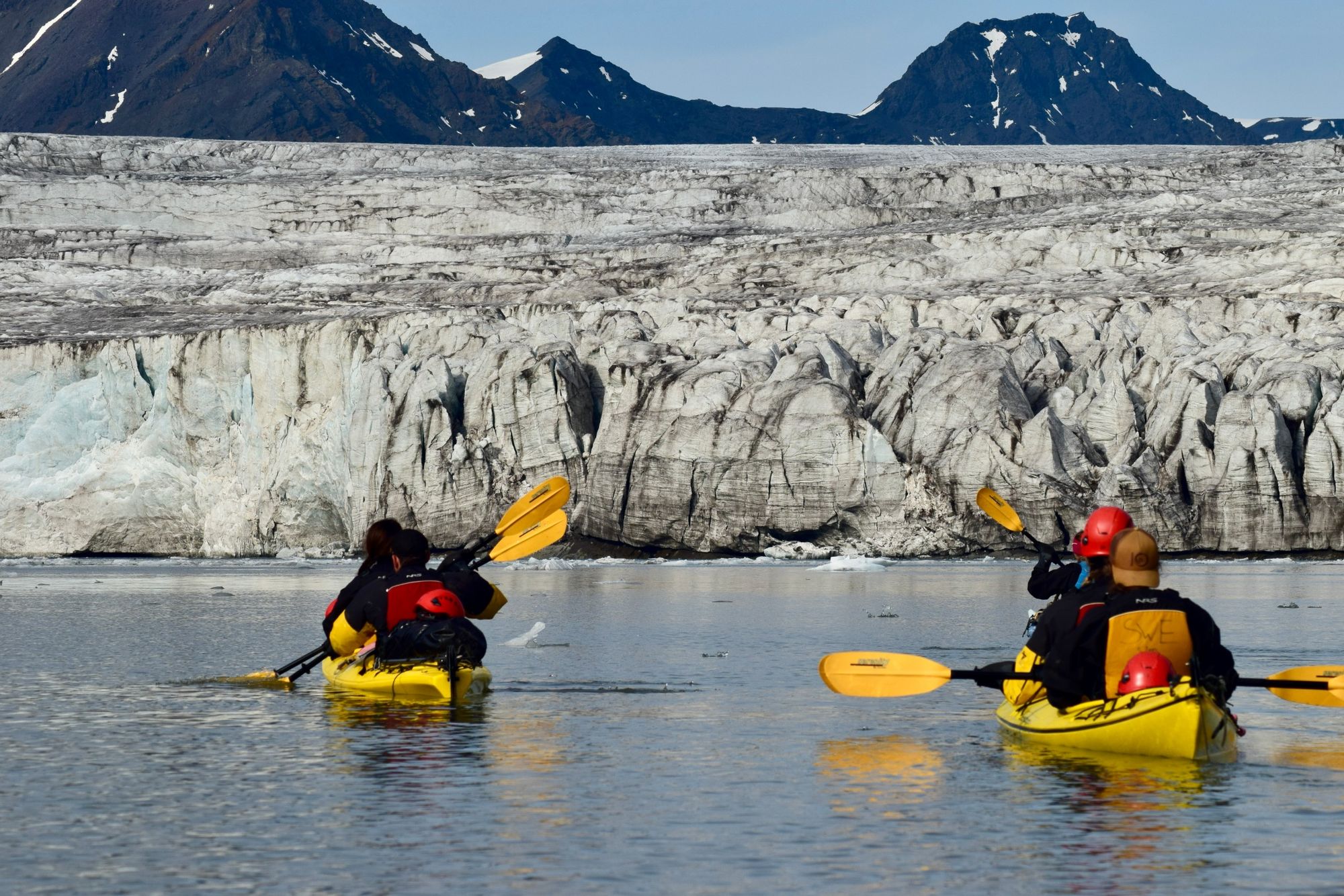 Multiple kayakers paddling towards the large ice wall of the Esmark Glacier.