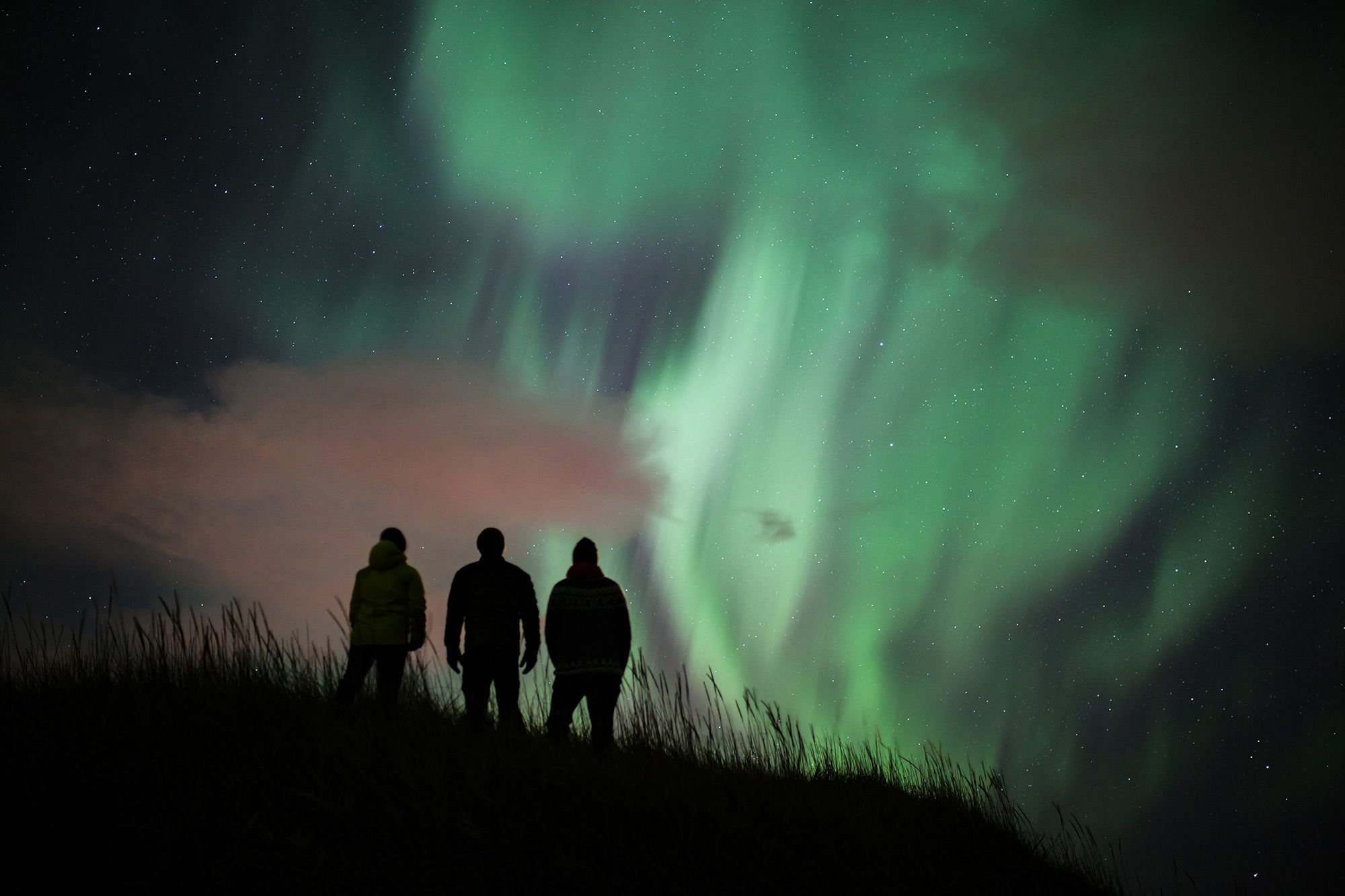 Three silhouetted figures watching the northern lights. Photo: Bjorgvin Hilmarsson.