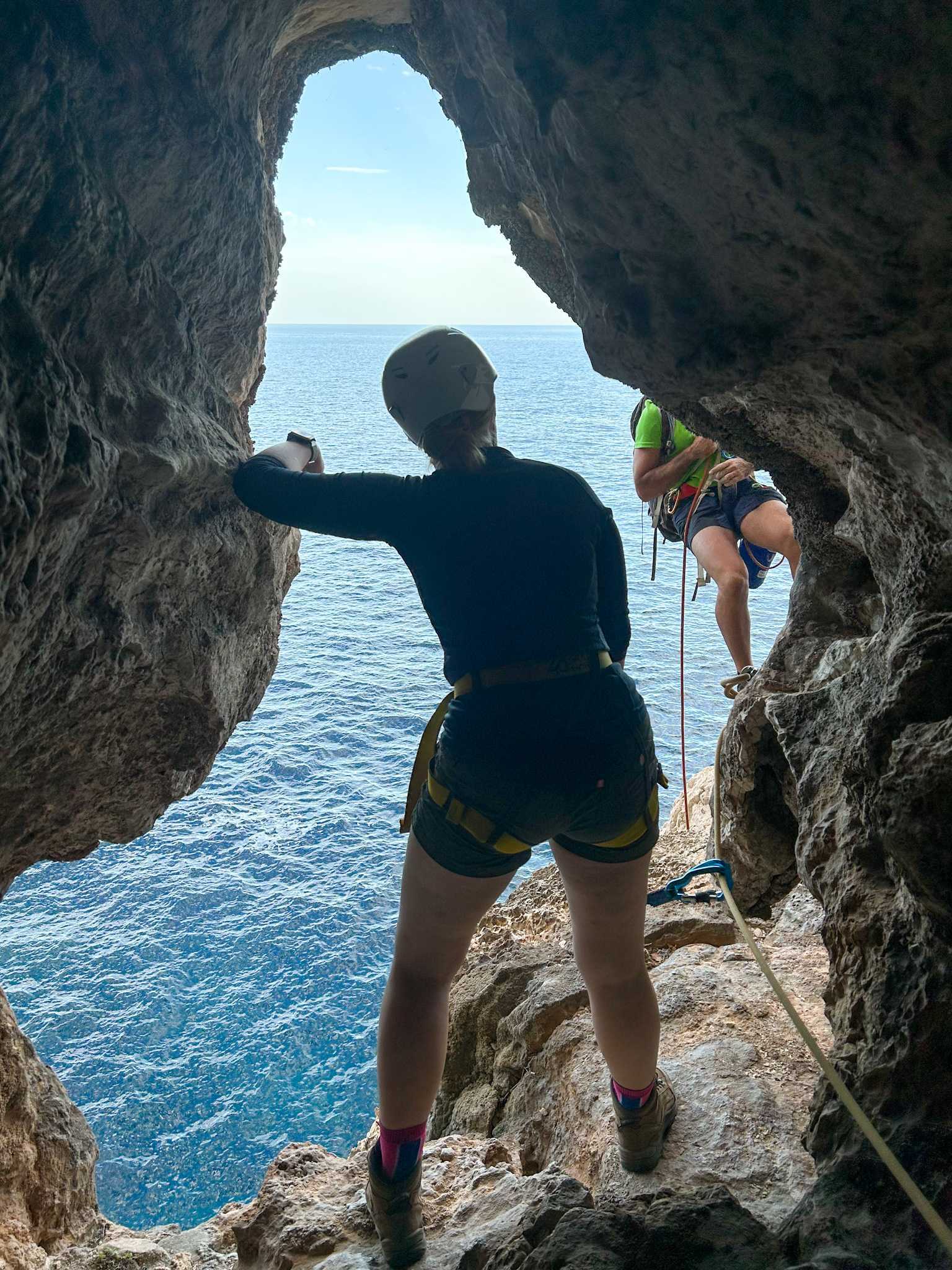 A roped climber in a cliffside cave, looking out to the sea, Sardinia.