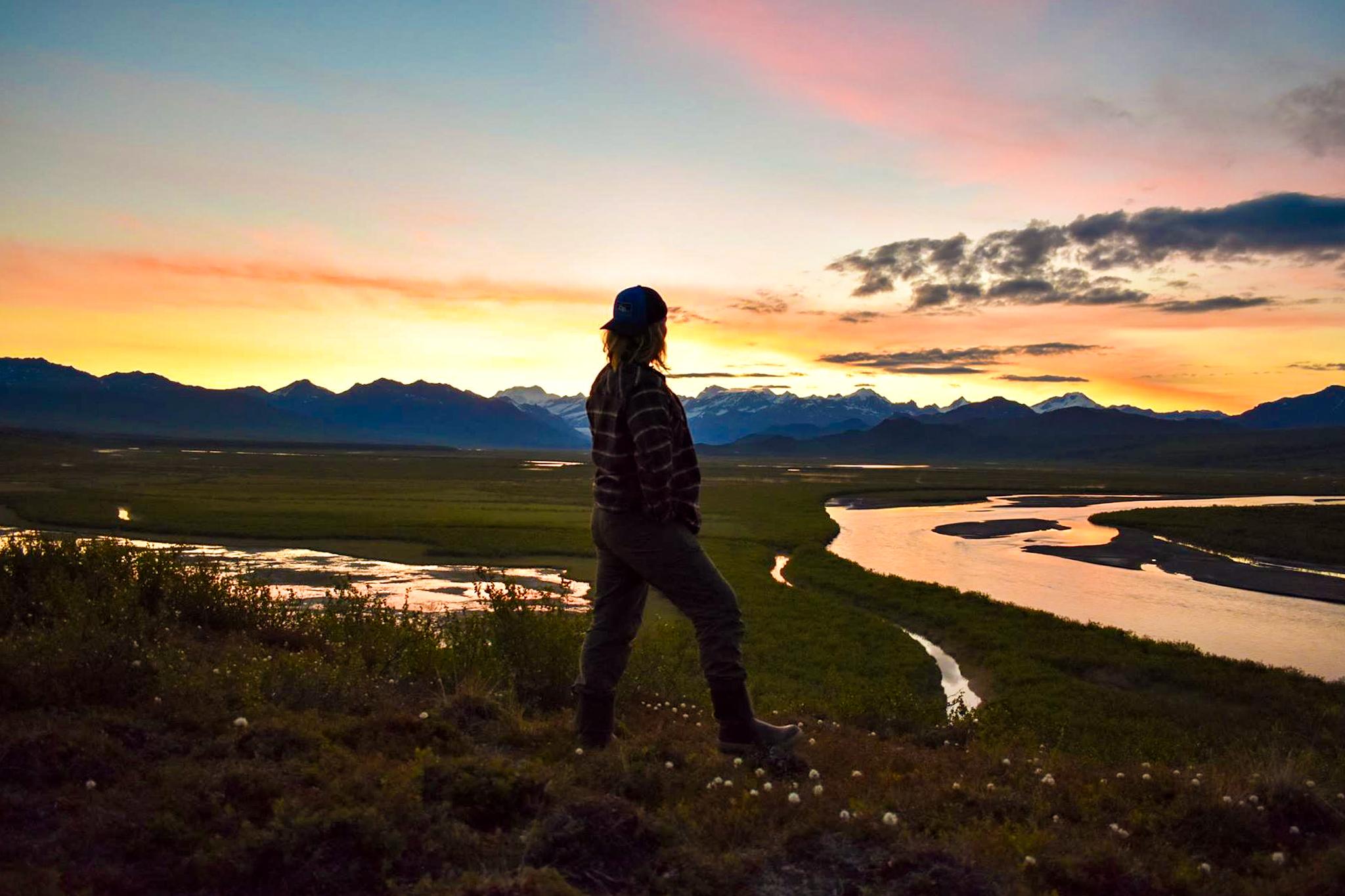 A hiker looking out over Maclaren River, Alaska, at sunset. Photo: Panagea Adventures.