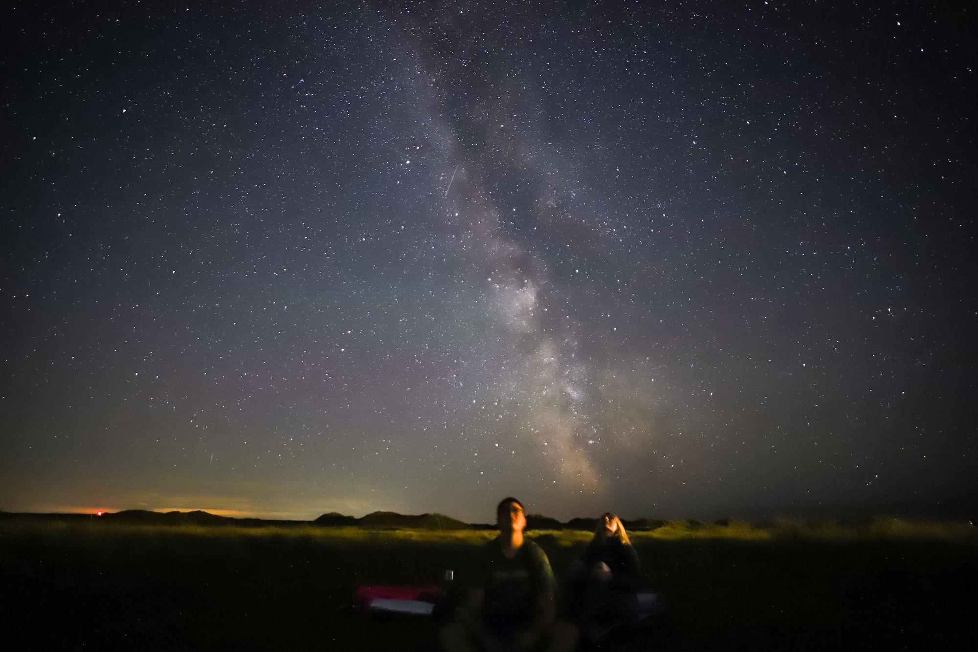 Two people sitting on the ground, looking up at the stars. Photo: Dani Robertson.