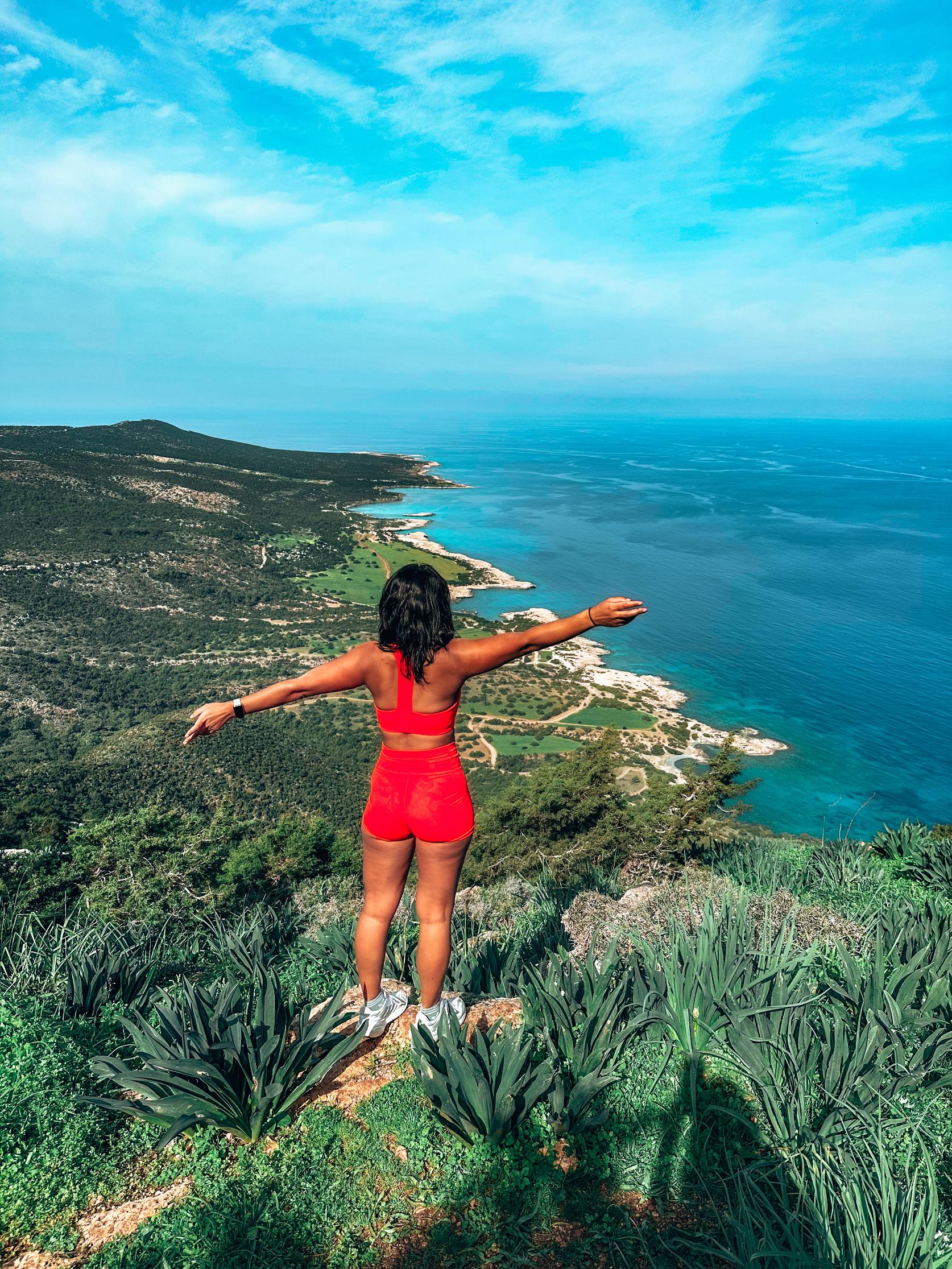 A woman looks out over the coast after hiking to a summit