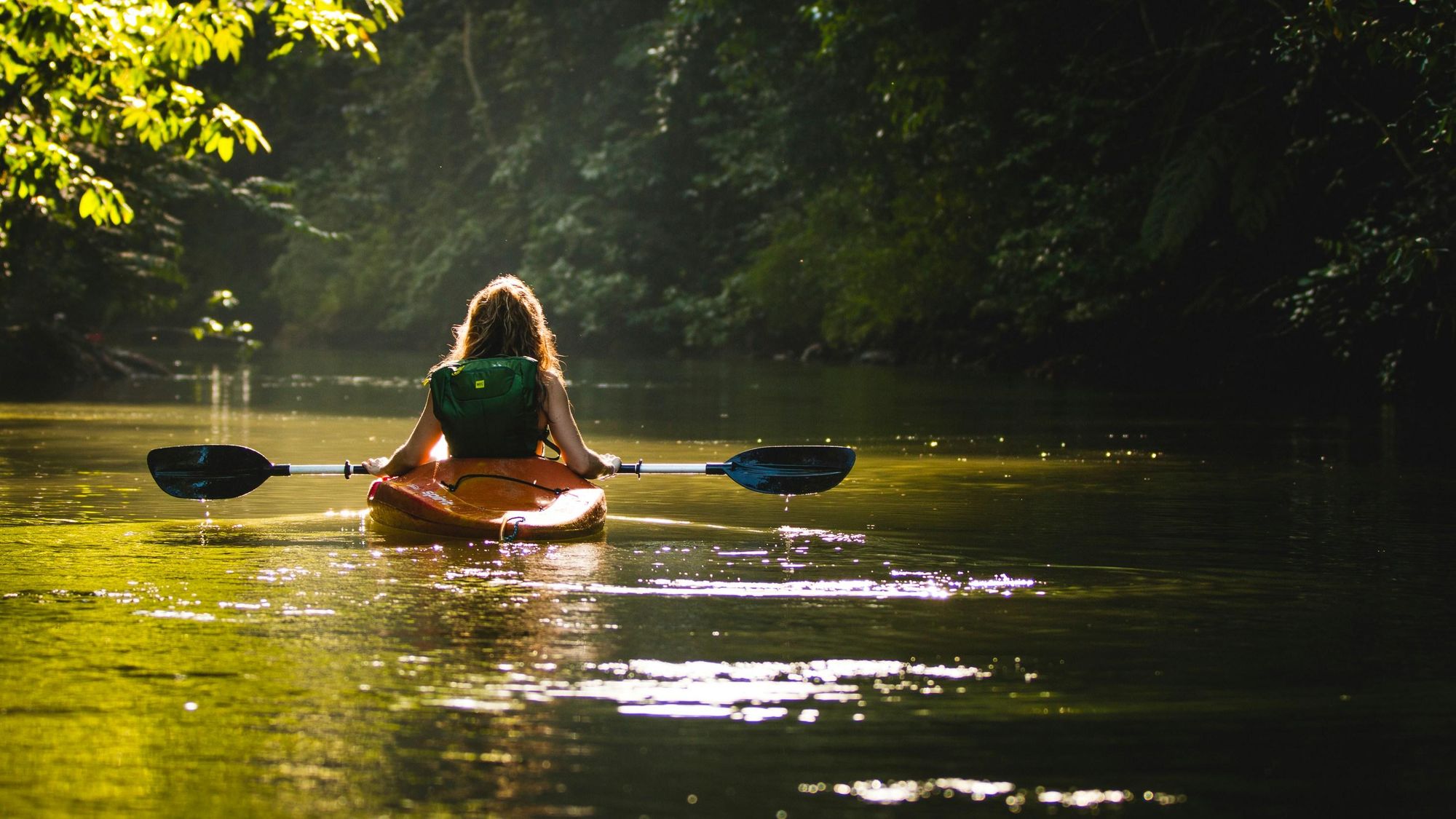 A woman finds a moment of tranquillity on a river flanked by forests. Photo: Filip Mroz/Unsplash