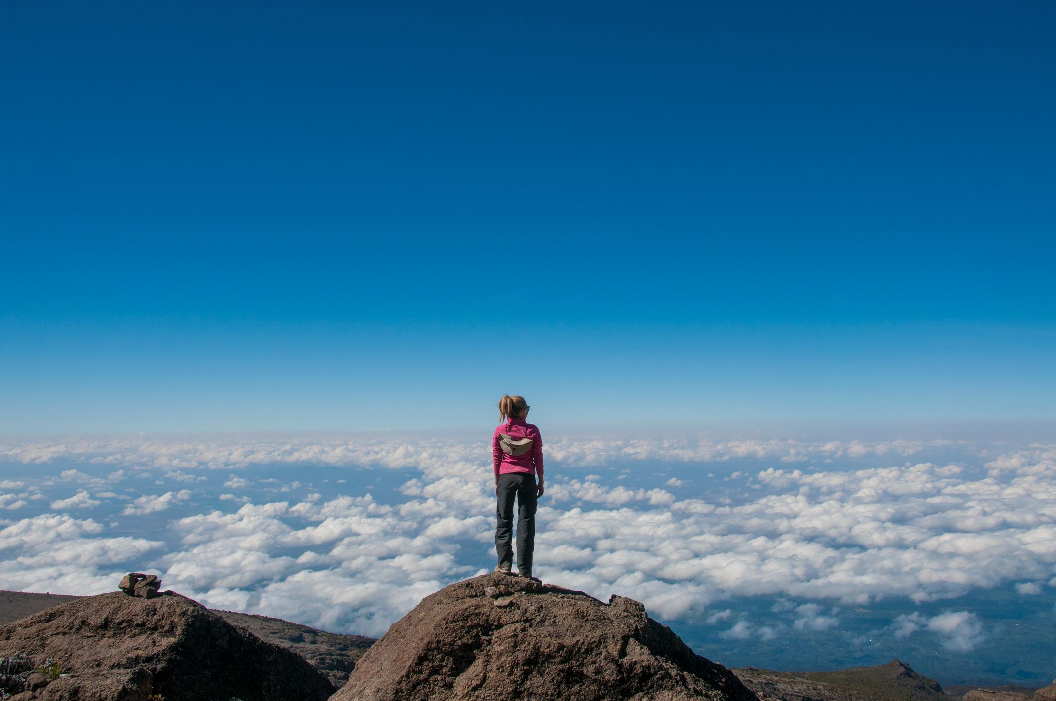 A woman looks out over a sea of clouds on Kilimanjaro summit.