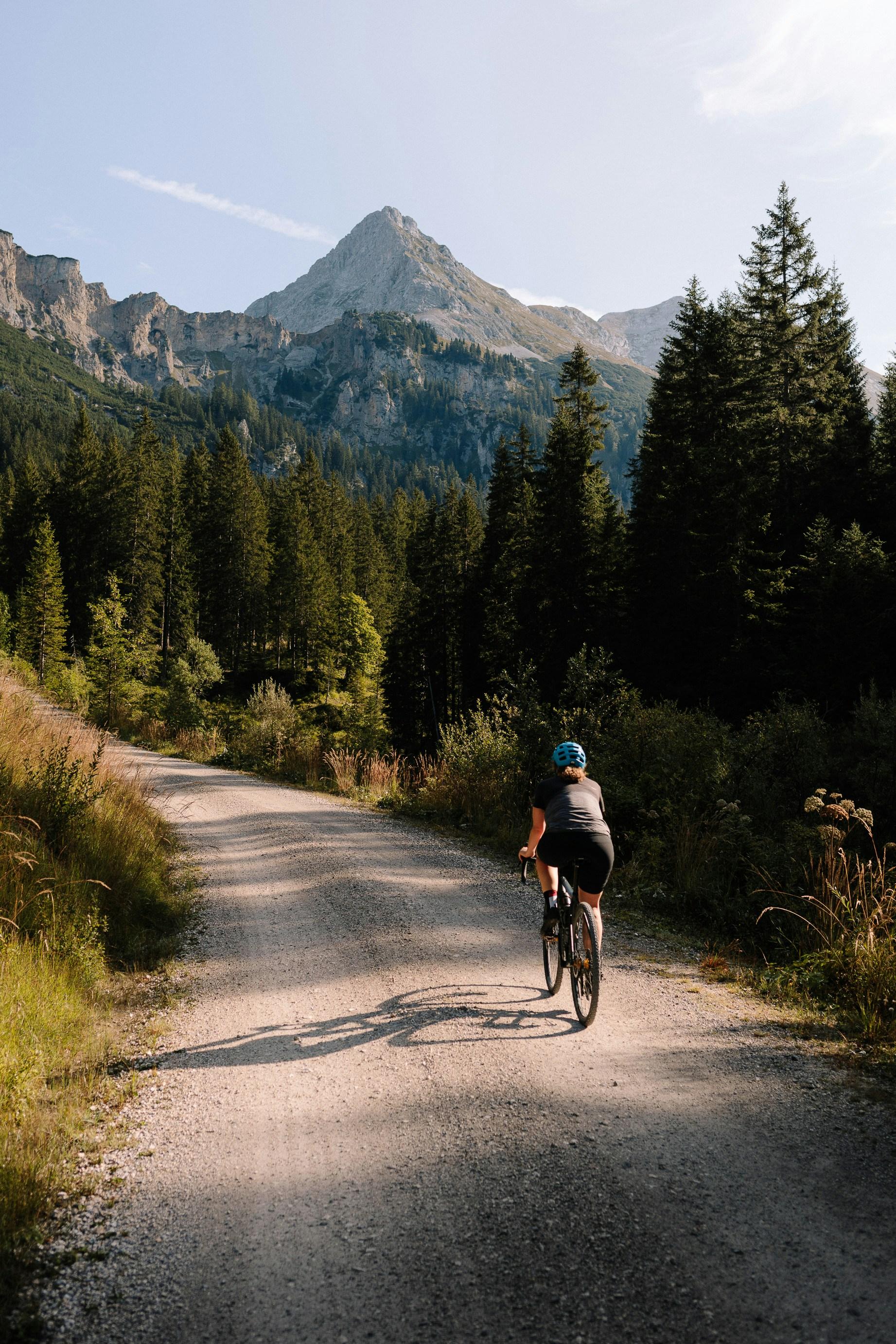 A woman on a gravel ride with a mountainous backdrop. Photo by Axel Brunst (via Unsplash)