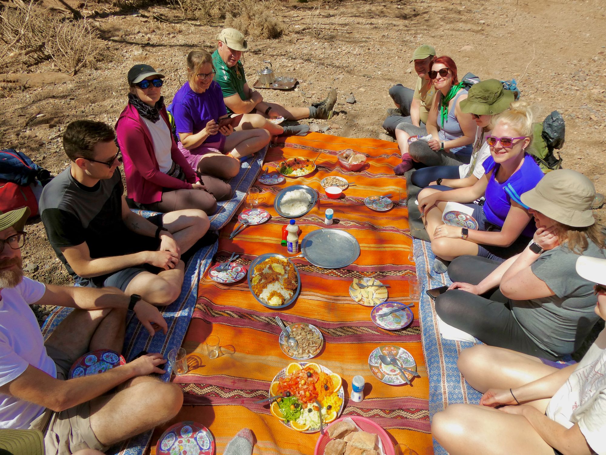 A group of people enjoying Moroccan food outdoors, on a colourful blanket.