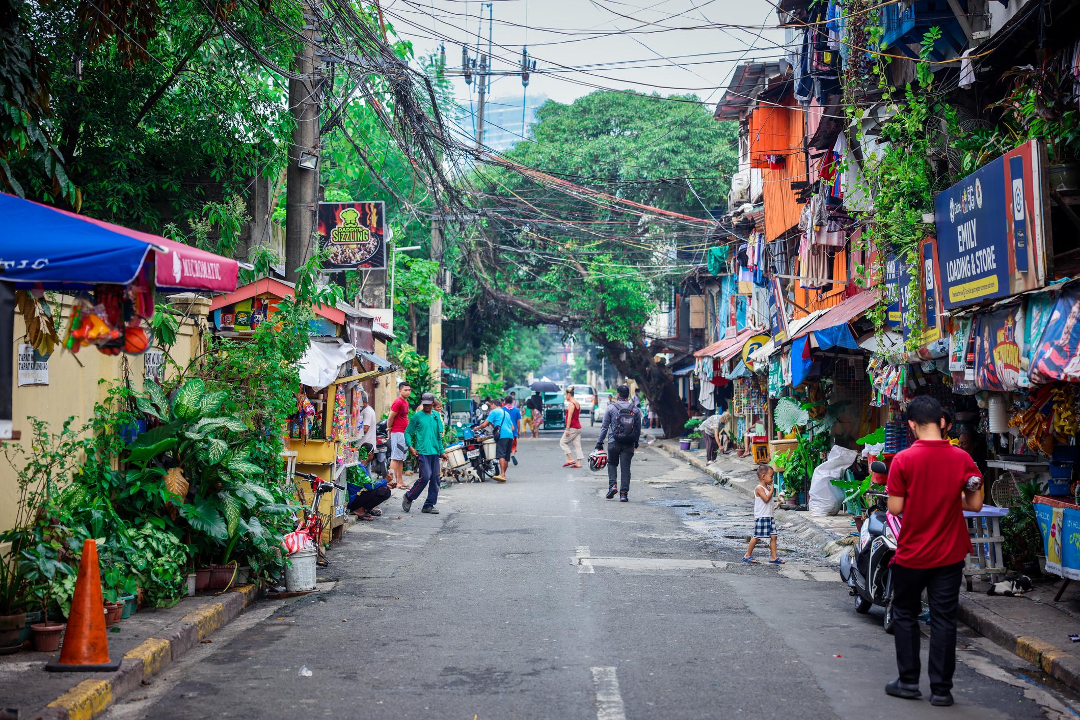 Locals walk along a lively street in Intramuros, Manila, filled with colourful stalls and greenery. Photo: Getty