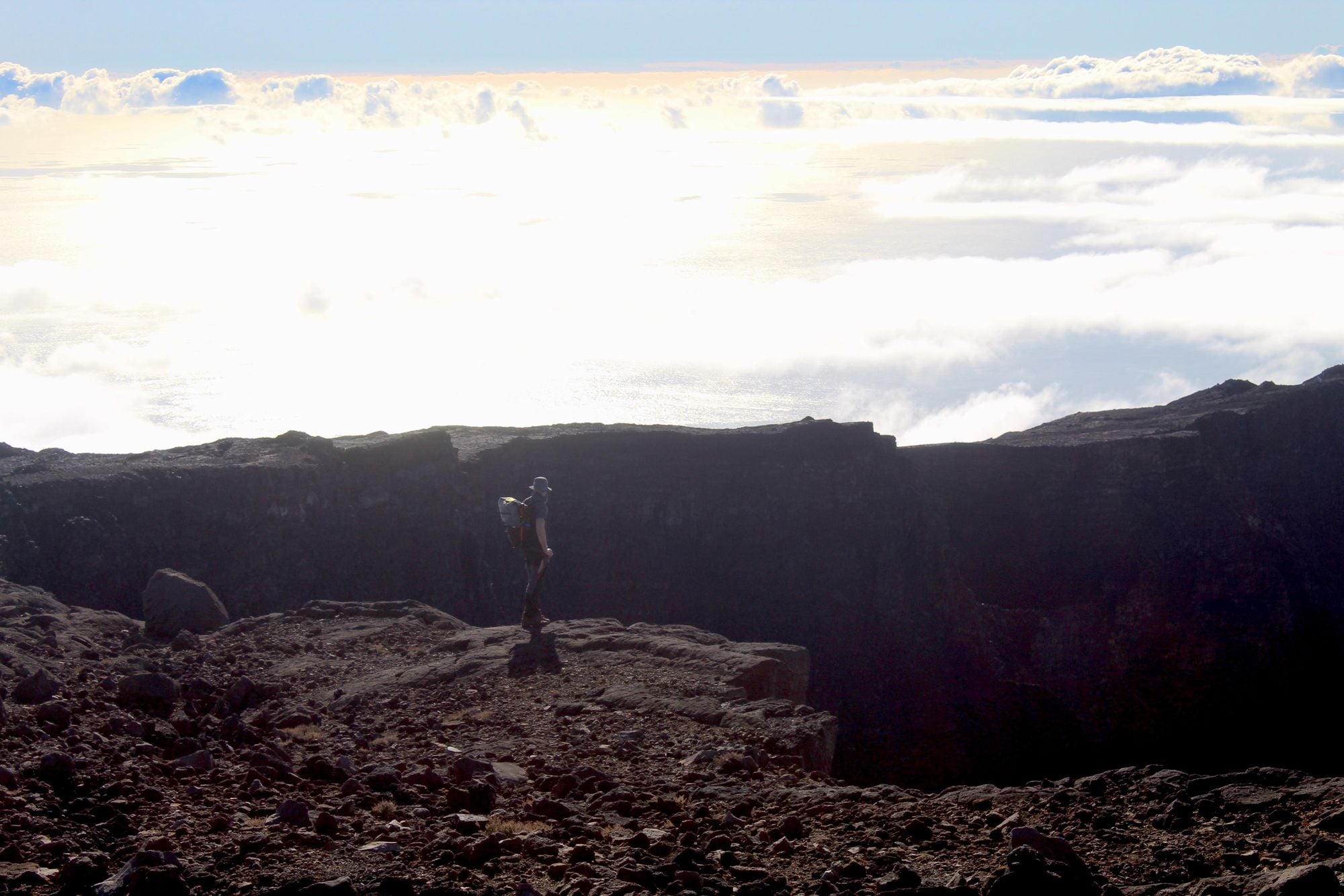 A hiker stands on the edge of the volcanic rim, with the blue of the sky and the water merging beyond. Photo: Stuart Kenny