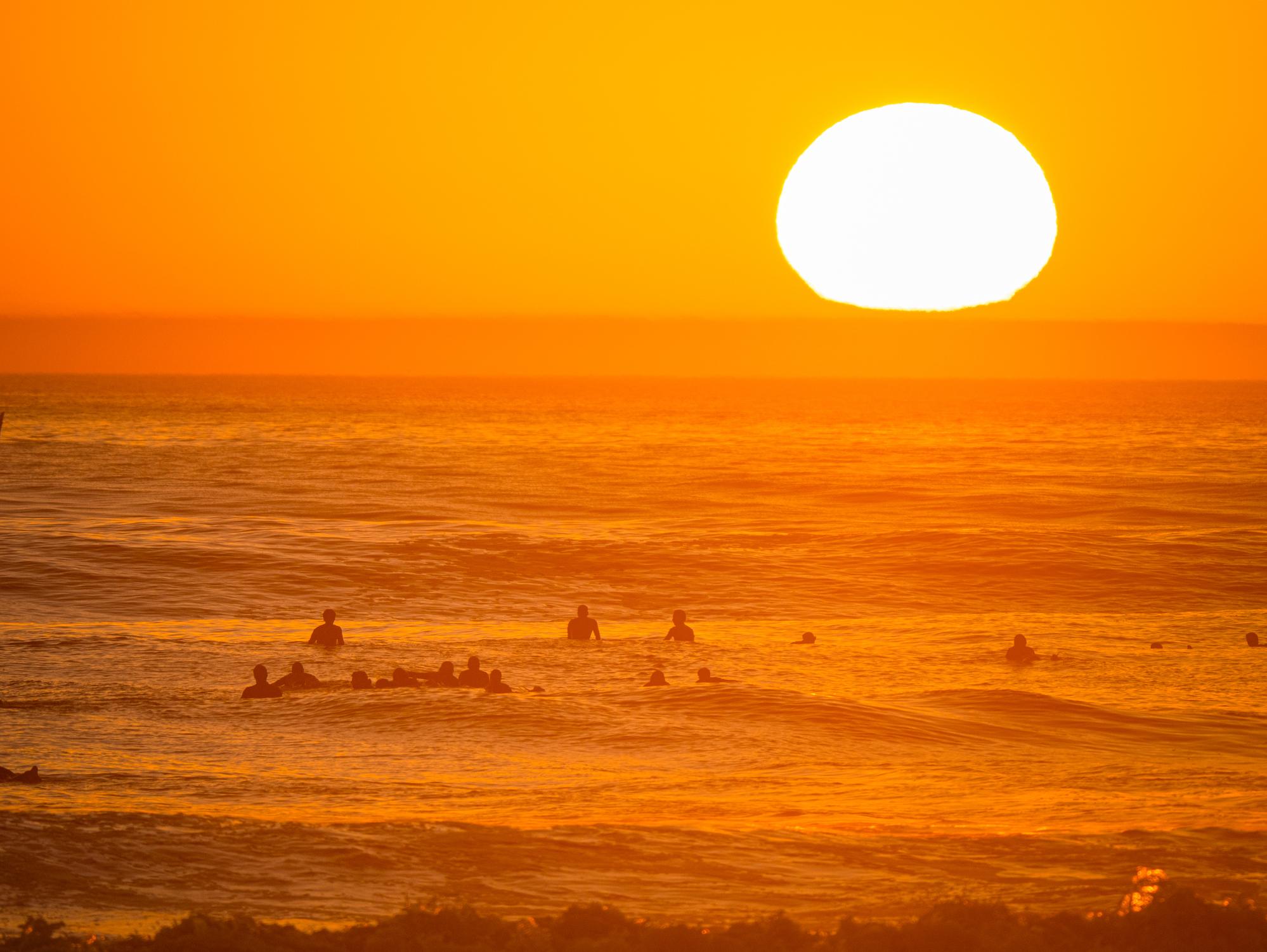 Surfers wait patiently in the ocean as the typical golden glow of Taghazout, Morocco sets over the surf. Photo: Getty
