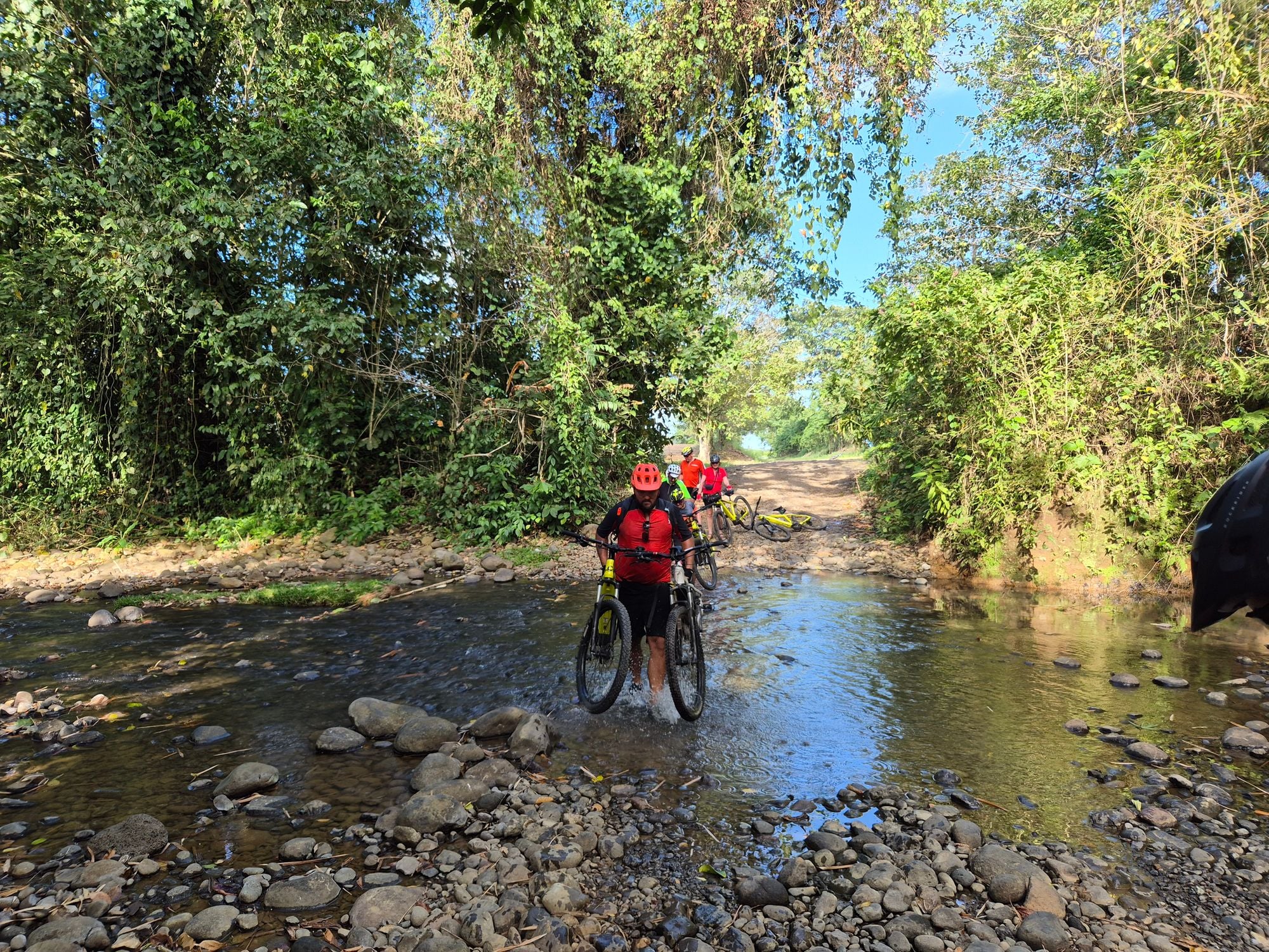 Cyclists carrying their e-bikes through a stream in Costa Rica.