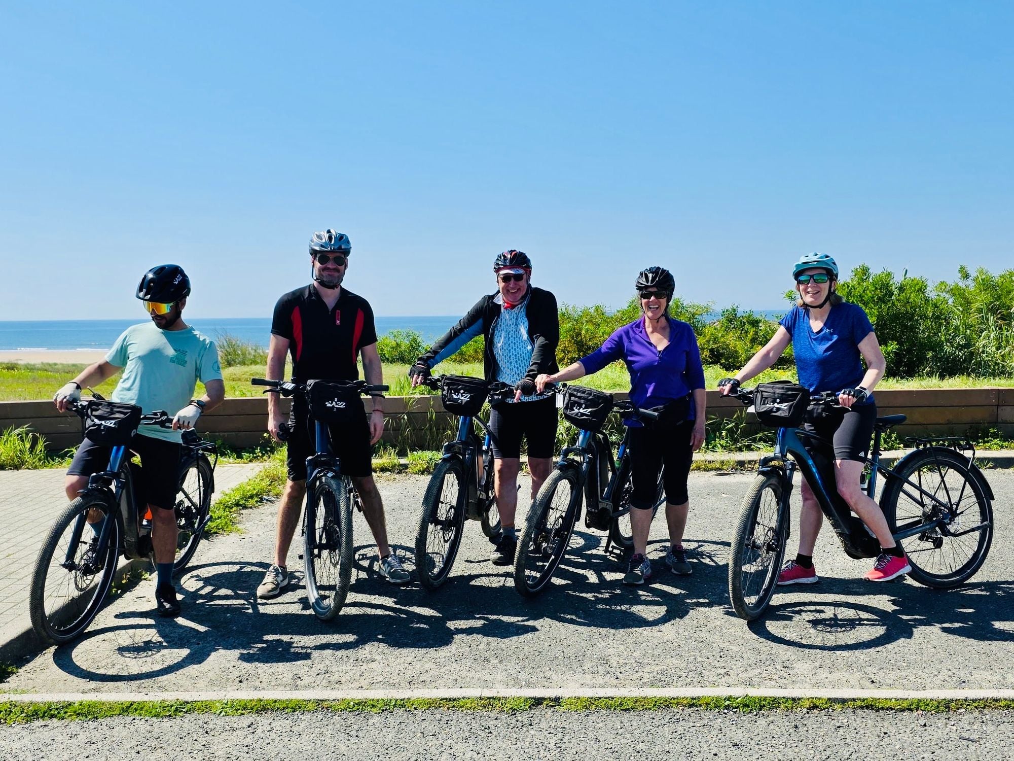 Five cyclists on e-bikes with the sea in the background.