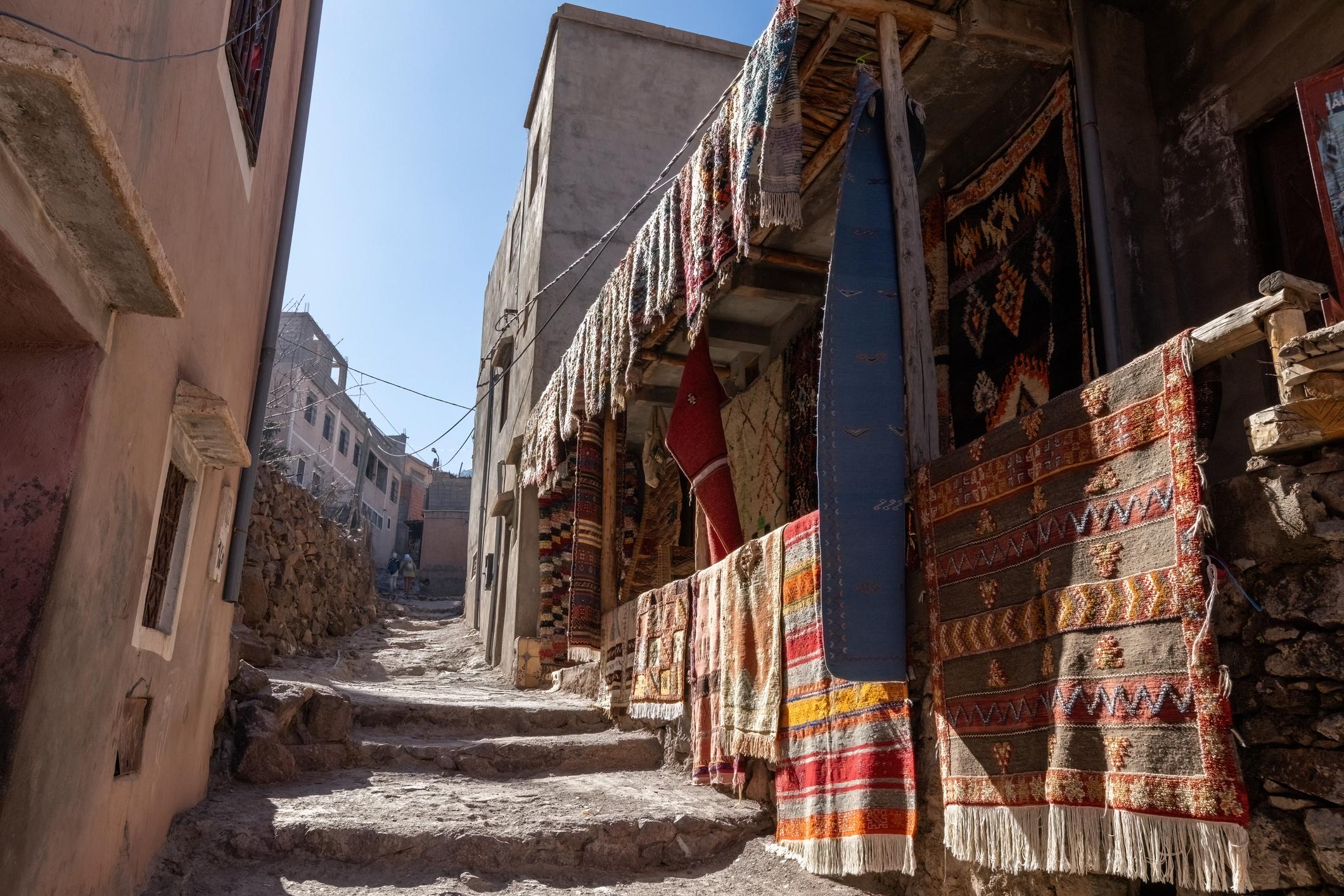 A narrow street in Imlil, with colourful, traditional rugs draped over one of the houses. Photo: Getty